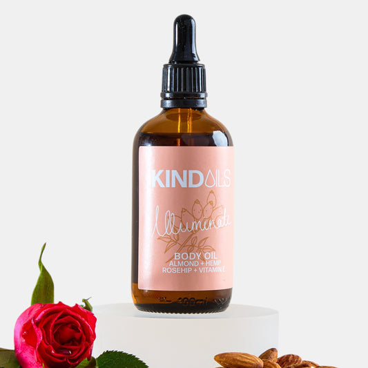Bottle of kind oils body oil with a rose and almonds on a white background