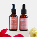 Two bottles of kind oils with rose petals and a white rose on a light background