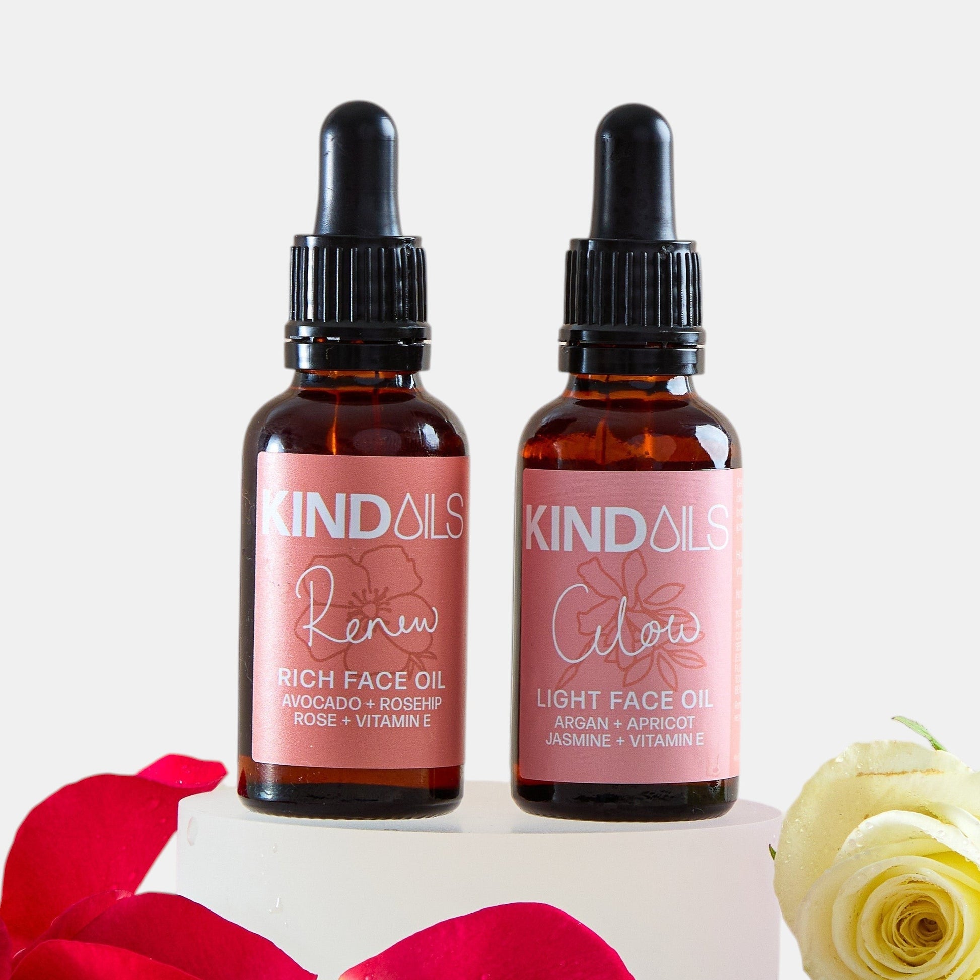 Two bottles of kind oils with rose petals and a white rose on a light background