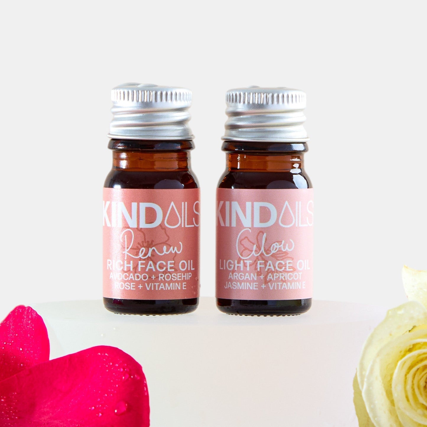 Two small bottles of KIND Oils with flowers on a white background