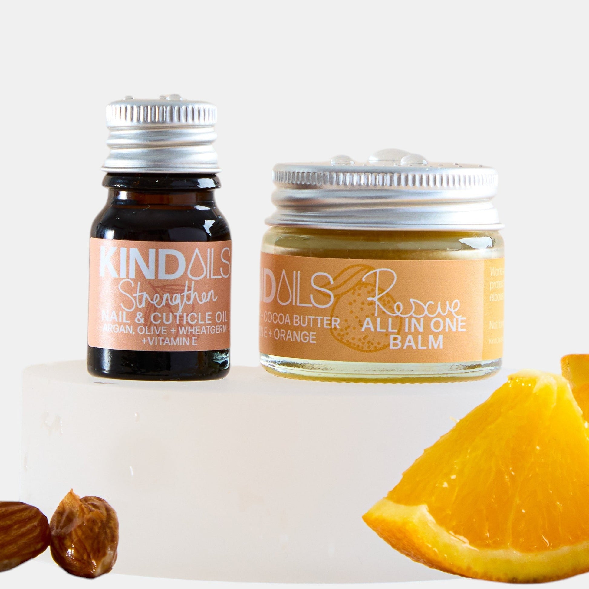 Two skincare products, a jar and a bottle, with orange slices and almonds on a white background.