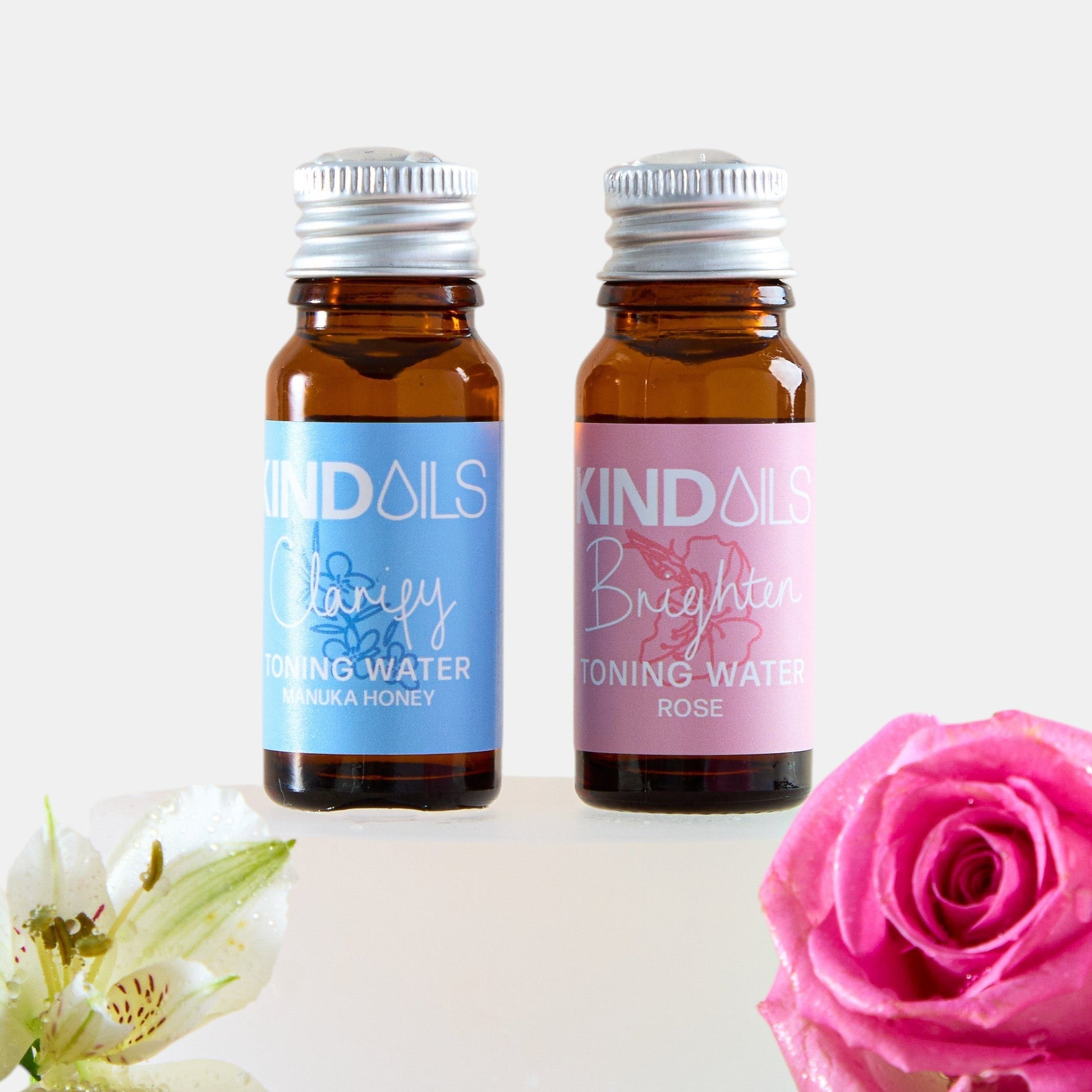 Two bottles of Kind Oils with flowers on a white background