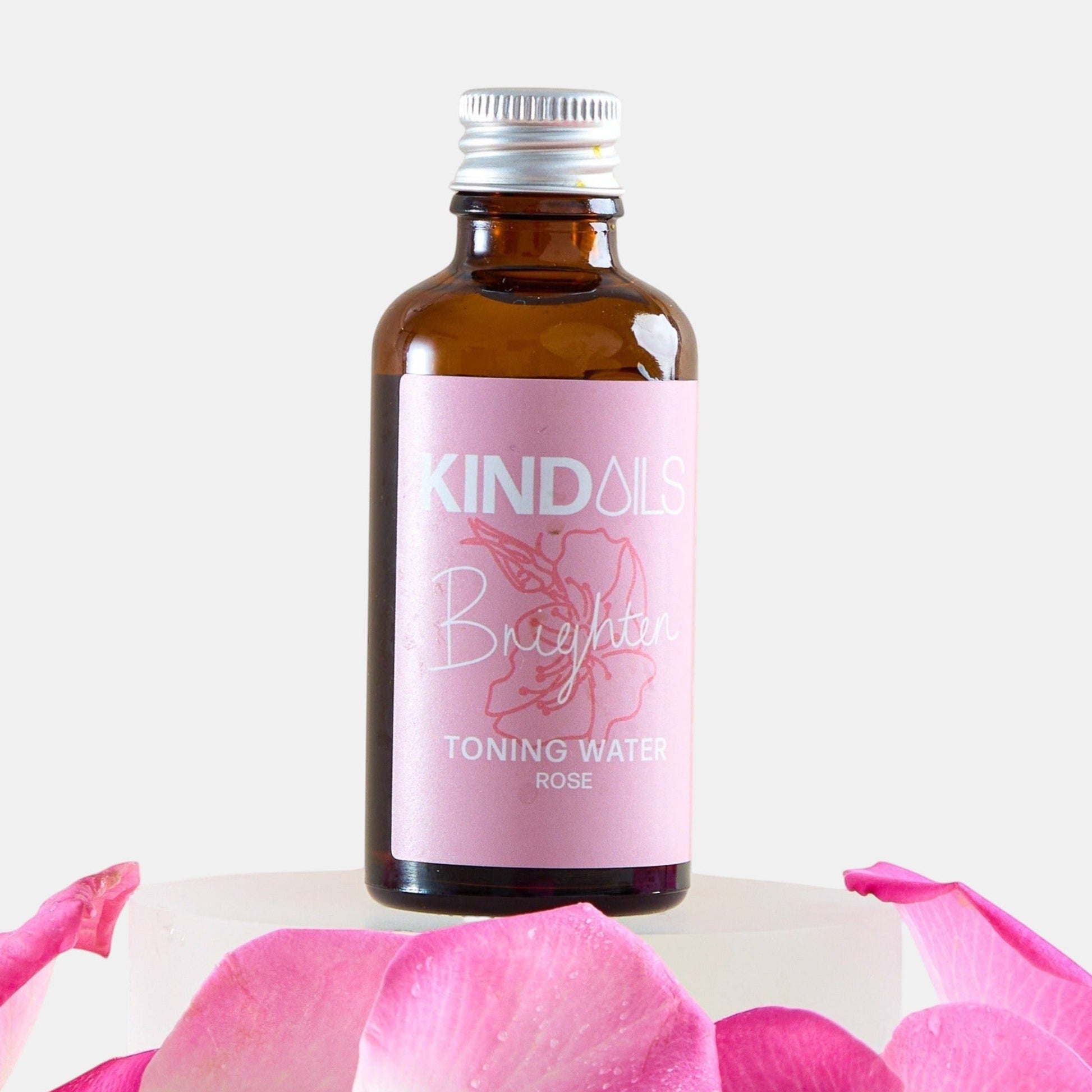 Bottle of kind oils Toning Water with pink label on a white background with pink petals.