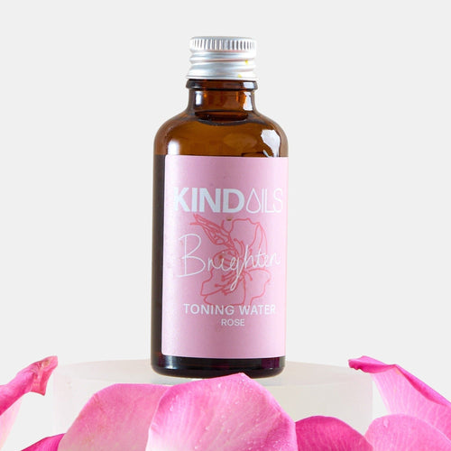 Bottle of kind oils Toning Water with pink label on a white background with pink petals.